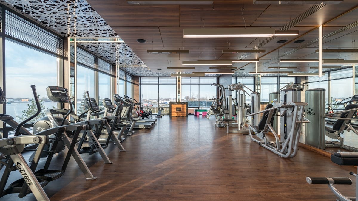 Interior of modern spacious fitness club with various sports machines and equipment placed on parquet floor near panoramic windows